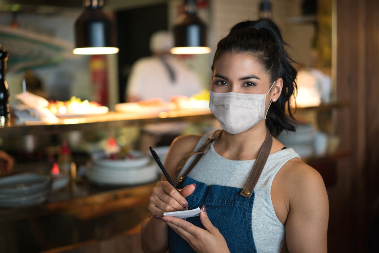 Beautiful waitress working at a restaurant wearing a facemask