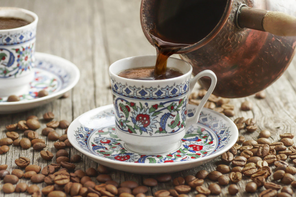 traditional turkish coffee in porcelain cup pouring from copper coffee pot, hot drink concept